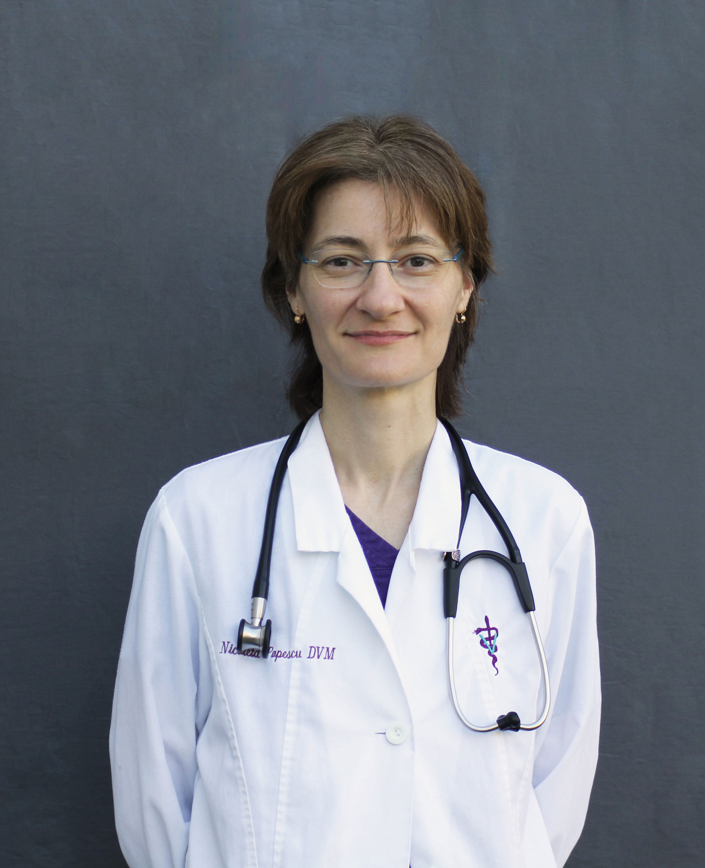Dr. Nicoleta Popescu, a tall, slim female veterinarian with short light brown hair smiles at the camera in a white lab coat.